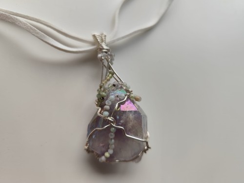 Ręcznie wykonany wisiorek z naturalnego ametystu, misternie opleciony drutem miedzianym pokrytym srebrem - widok z góry na wisiorek.
