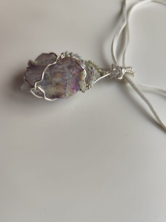Ręcznie wykonany wisiorek z naturalnego ametystu, misternie opleciony drutem miedzianym pokrytym srebrem - widok pod kątem na wisiorek.