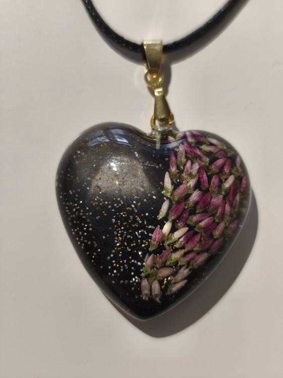 Zawieszka w kształcie serca z nasionami wrzosu i brokatem zatopionymi w ciemnej żywicy - zbliżenie