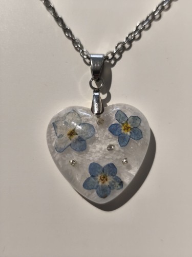 Zawieszka w kształcie serca z suszonymi niezapominajkami zatopionymi w jasnej żywicy - zbliżenie
