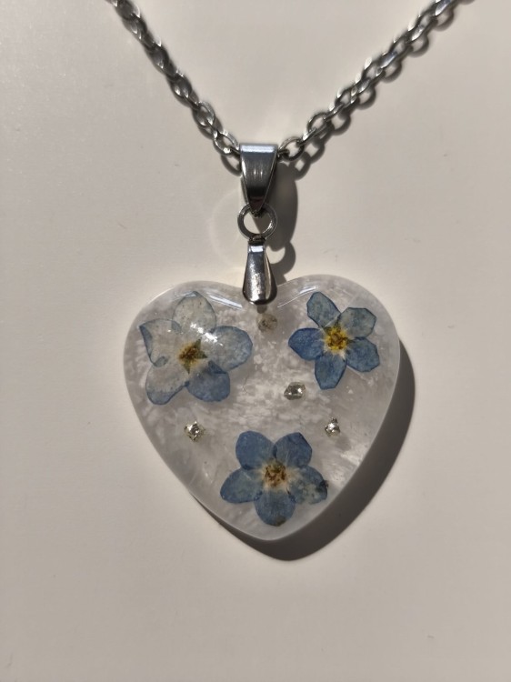 Zawieszka w kształcie serca z suszonymi niezapominajkami zatopionymi w jasnej żywicy - zbliżenie